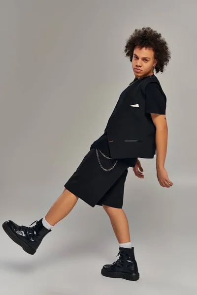 Hübsches afrikanisch-amerikanisches männliches Model in schwarzer stylischer Kleidung posiert aktiv vor grauem Hintergrund — Stockfoto