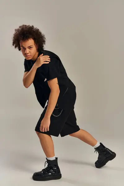 Handsome african american male model in urban stylish attire posing actively on gray backdrop — Stock Photo