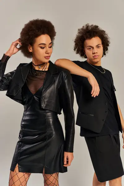 Joven afroamericano hermano y hermana en vívida ropa posando juntos en gris telón de fondo - foto de stock