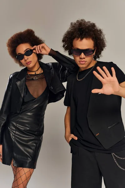 Attrayants frères et sœurs afro-américains en tenue noire à la mode avec des lunettes de soleil posant sur fond gris — Photo de stock