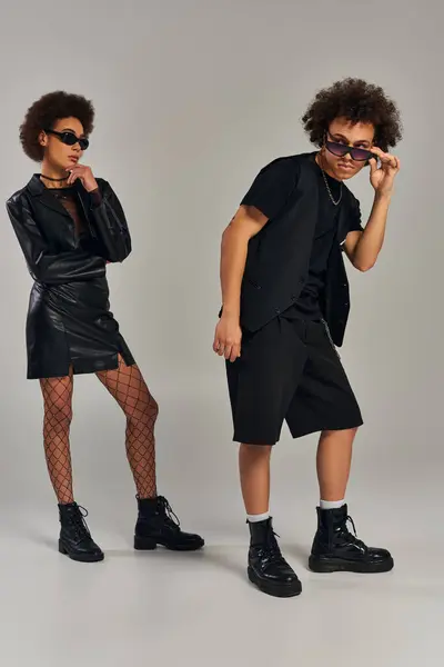 Giovani fratelli afroamericani in abbigliamento nero alla moda con occhiali da sole in posa su sfondo grigio — Foto stock