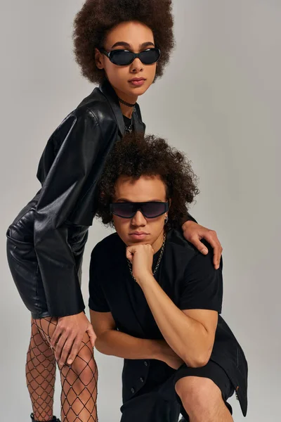 Frères et sœurs afro-américains à la mode en tenue noire élégante avec des lunettes de soleil posant sur fond gris — Photo de stock