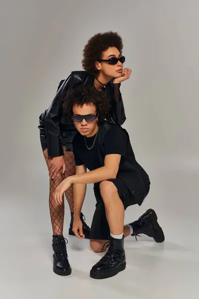 Stylish african american siblings in trendy black attire with sunglasses posing on gray backdrop — Stock Photo