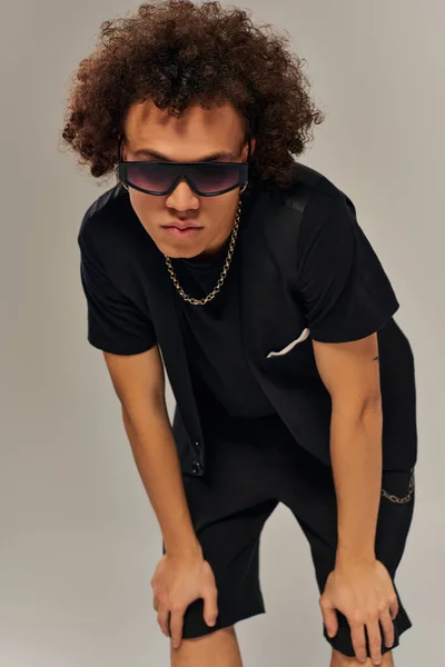 Atractivo modelo masculino afroamericano de moda con gafas de sol elegantes posando activamente en la cámara - foto de stock