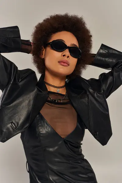 Портрет модной африканской американки в солнцезащитных очках и стильной одежде на сером фоне — стоковое фото