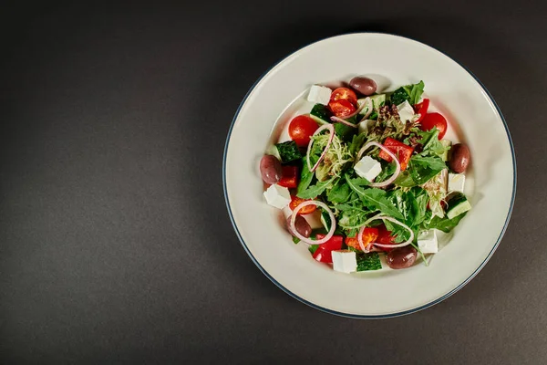 Foto von oben von Teller mit frisch zubereitetem köstlichen griechischen Salat auf grauem Hintergrund, gesunde Ernährung — Stockfoto