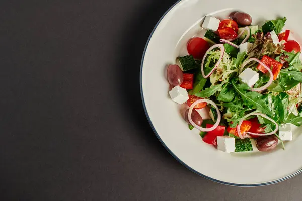 Вид сверху фото тарелки со свежим и вкусным греческим салатом на сером фоне, здоровое питание — стоковое фото