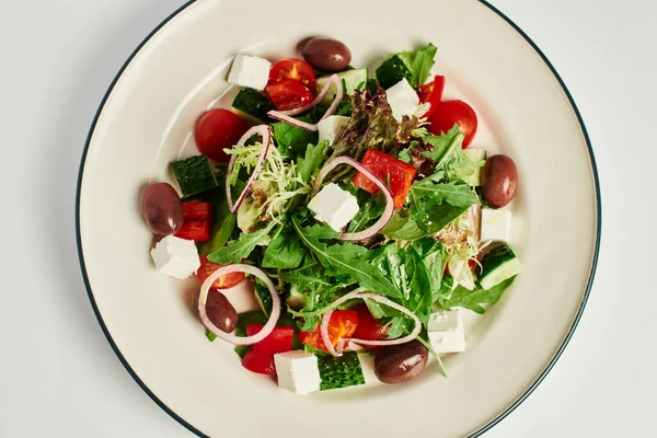 Вид зверху фото тарілки зі свіжим смачним грецьким салатом на сірому фоні, здорове харчування — стокове фото