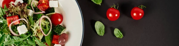 Foto vista dall'alto del piatto con insalata greca tradizionale vicino ai pomodorini su sfondo nero, banner — Foto stock