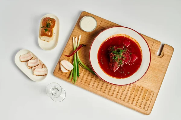 Traditional Ukrainian beetroot soup near garlic buns, pork lard and sour cream on cutting board — Stock Photo