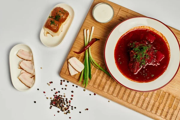 Traditional Ukrainian borsch near garlic buns, pork lard and sour cream on cutting board, top view — Stock Photo