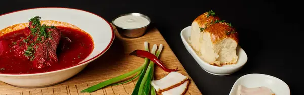 Смачний український борщ біля часникових булочок, свинячого салату та зеленої цибулі на обробній дошці, банер — стокове фото