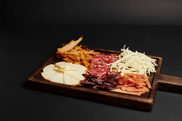 Charcuterie board with cheese selection, dried beef and salami slices on wooden cutting board — Stock Photo