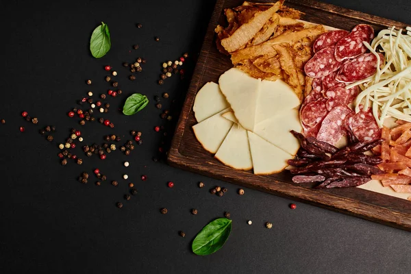 Vista superior da placa de charcutaria com deliciosa seleção de queijo, carne seca e fatias de salame em preto — Fotografia de Stock