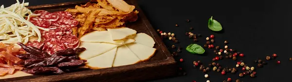 Tabla de charcutería con selección de queso gourmet, carne seca y rebanadas de salami en negro, pancarta - foto de stock