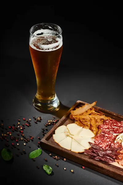 Стакан ремесленного пива рядом с доской для гурманов с сыром, сушеной говядиной и салями на борту — стоковое фото