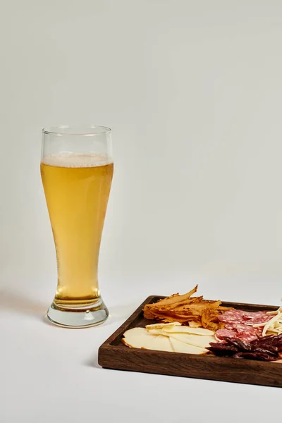 Bicchiere di birra artigianale vicino tagliere con selezione di formaggi, manzo essiccato e salame su grigio — Foto stock