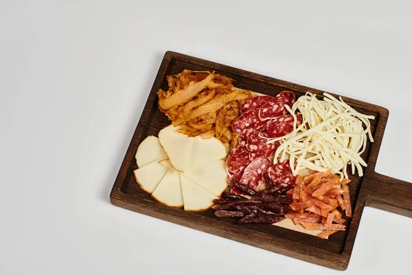 Доска для вечеринок с блюдом из сыра для гурманов, сушеной говядиной и ломтиками салями на сером фоне — стоковое фото