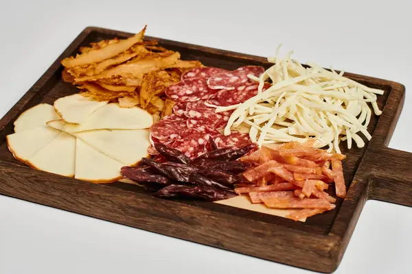 Planche de charcuterie avec plateau de fromage savoureux, boeuf séché et tranches de salami sur fond gris — Photo de stock