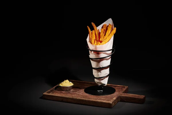 Comfort food, patatine fritte croccanti all'interno del cono di carta vicino salsa intingente sul tagliere di legno — Foto stock