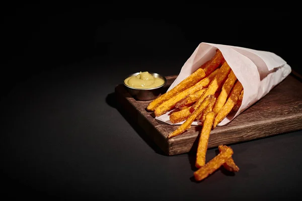 Repas rapide, frites croustillantes à l'intérieur du cône de papier près de sauce à tremper sur planche à découper en bois — Photo de stock