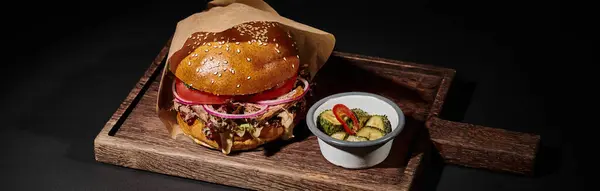 Deliciosa hamburguesa con pan de sésamo, carne de res y encurtidos como guarnición en bandeja de madera en negro, pancarta - foto de stock