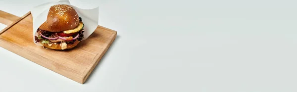 Hamburger juteux avec bœuf grillé, oignon rouge, fromage fondu et pain au sésame sur planche de bois, bannière — Photo de stock