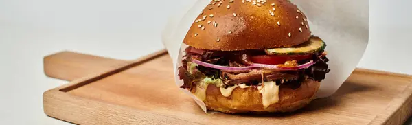 Hamburger con carne alla griglia, cipolla rossa, formaggio fuso e panino al sesamo sul tagliere di legno, striscione — Foto stock