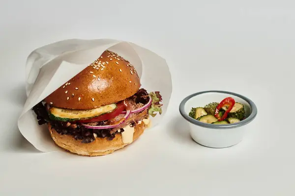 Délicieux hamburger avec pain de sésame, bœuf et cornichons comme plat d'accompagnement sur plateau en bois sur fond gris — Photo de stock