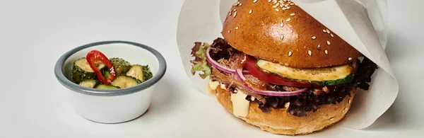 Pancarta de hamburguesa con pan de sésamo, carne de res y encurtidos como guarnición en bandeja de madera sobre fondo gris - foto de stock