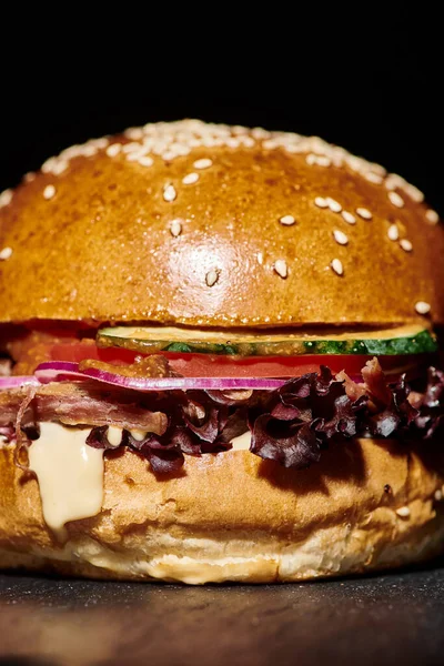 Gustoso hamburger con pancetta, cipolla rossa, formaggio fuso e panino al sesamo su sfondo nero, primo piano — Foto stock