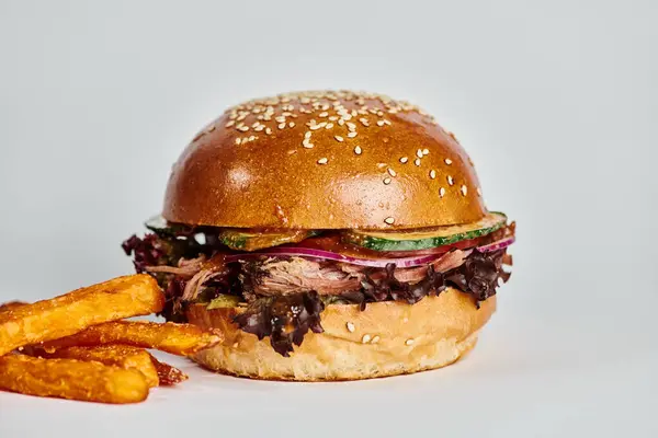 Gustoso hamburger con carne di manzo, cipolla rossa, pomodoro e panino al sesamo vicino alle patatine fritte su sfondo grigio — Foto stock