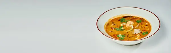 Гострий тайський суп з кокосовим молоком, креветками, лимонником та кінзою на сірому фоні, банер Тома смаку — стокове фото