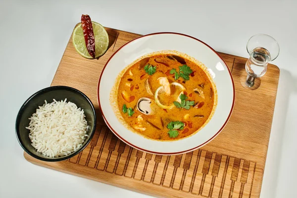 Thai soup with coconut milk, shrimp, lemongrass and cilantro near rice bowl on grey, Tom yum — Stock Photo