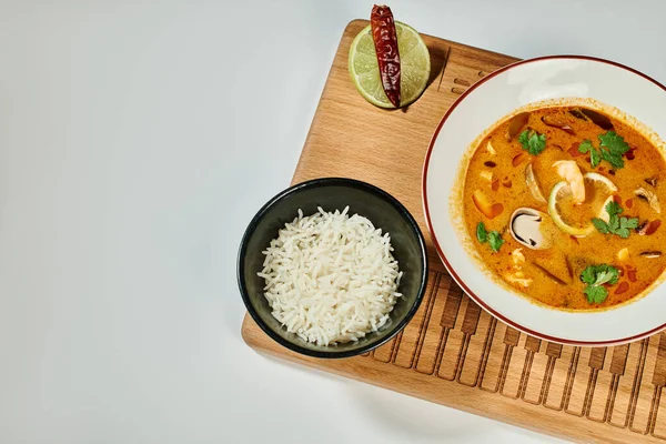 Tom yum soup with coconut milk, shrimp, lemongrass and cilantro near rice bowl on grey background — Stock Photo