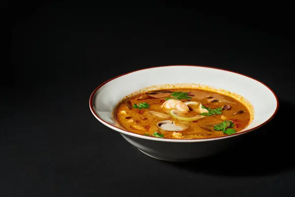 Würzige Tom-Yum-Suppe mit Kokosmilch, Garnelen, Zitronengras und Koriander auf schwarzem Hintergrund. Nahaufnahme — Stockfoto