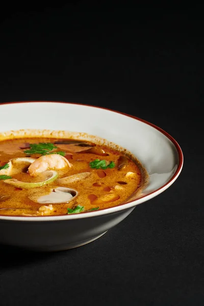 Sopa picante Tom yum com leite de coco, camarão, erva-cidreira e coentro no fundo preto, close up — Fotografia de Stock