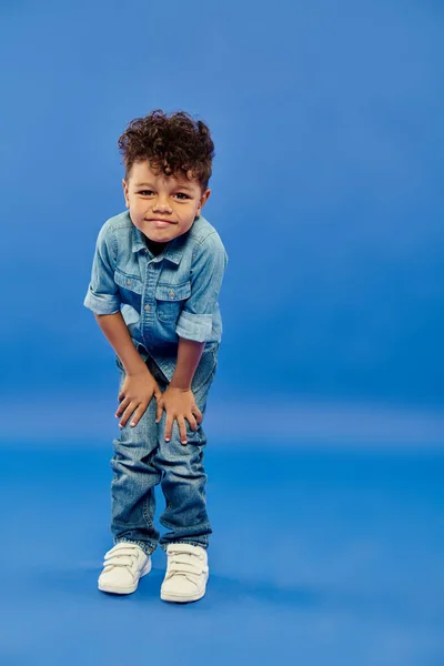 Little curly african american preschooler boy in stylish denim outfit posing on blue background — Stock Photo