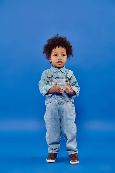 Adorável e encaracolado afro-americano criança menino em denim roupas de pé no fundo azul — Fotografia de Stock