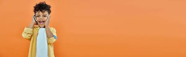 Heureux garçon préscolaire afro-américain en tenue décontractée parler sur smartphone sur orange, bannière — Photo de stock