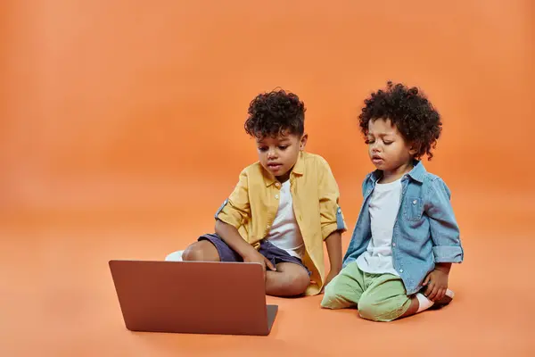 Entzückende afrikanisch-amerikanische Geschwister in lässiger Sommerkleidung sehen Film auf Laptop, orangefarbener Hintergrund — Stockfoto