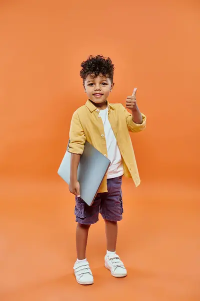 Felice e riccio ragazzo afroamericano mostrando come e tenendo il computer portatile su sfondo arancione — Foto stock