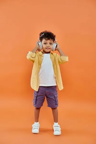 Fröhlicher und lockiger afrikanischer Junge, der Musik in drahtlosen Kopfhörern auf orangefarbenem Hintergrund hört — Stockfoto