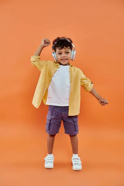 Garçon afro-américain souriant et bouclé écoutant de la musique dans des écouteurs sans fil sur fond orange — Photo de stock