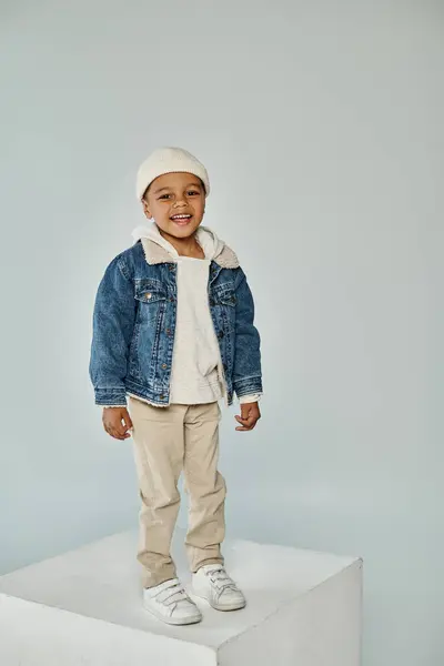Cheerful african american preschooler boy in winter attire and beanie hat on grey backdrop — Stock Photo