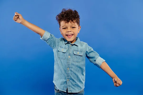 Portrait of excited african american boy in denim attire looking at camera on blue background — Stock Photo