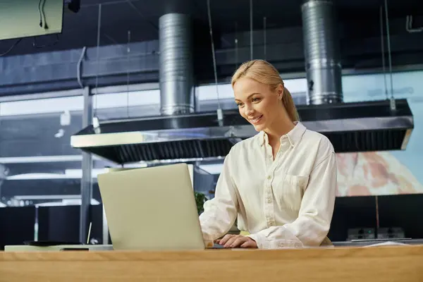 Positive gestionnaire blonde élégant travaillant sur ordinateur portable sur le comptoir dans le café moderne, l'industrie hôtelière — Photo de stock
