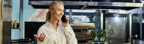 Excité administrateur blonde parler sur téléphone mobile et gestuelle dans un café moderne, bannière horizontale — Photo de stock
