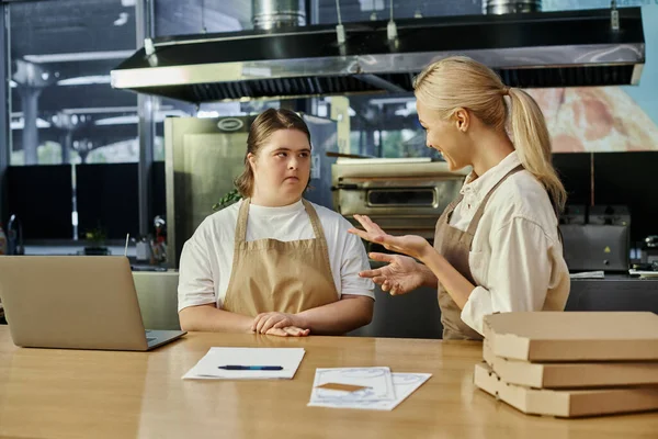Glücklicher Café-Manager erklärt junge Frau mit Down-Syndrom in der Nähe von Laptop und Pizzakartons ihre Pflichten — Stockfoto