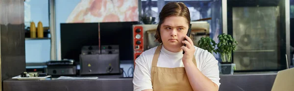 Mujer joven con síndrome de Down hablando por teléfono móvil mientras trabaja en la cafetería moderna, pancarta - foto de stock